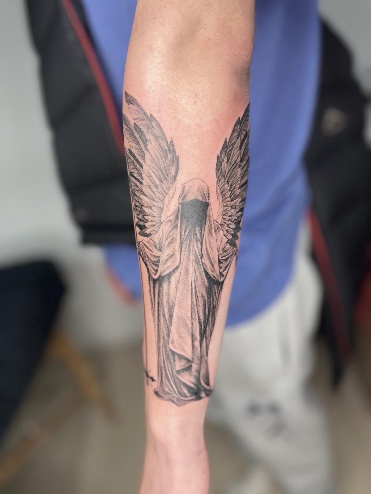 Black-and-grey hooded winged angel tattoo on a forearm
