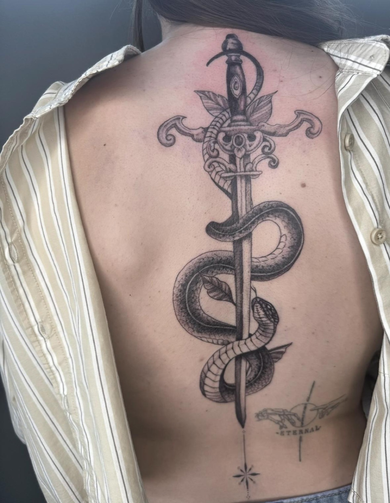 Fineline dagger entwined with a snake, tattooed along the spine